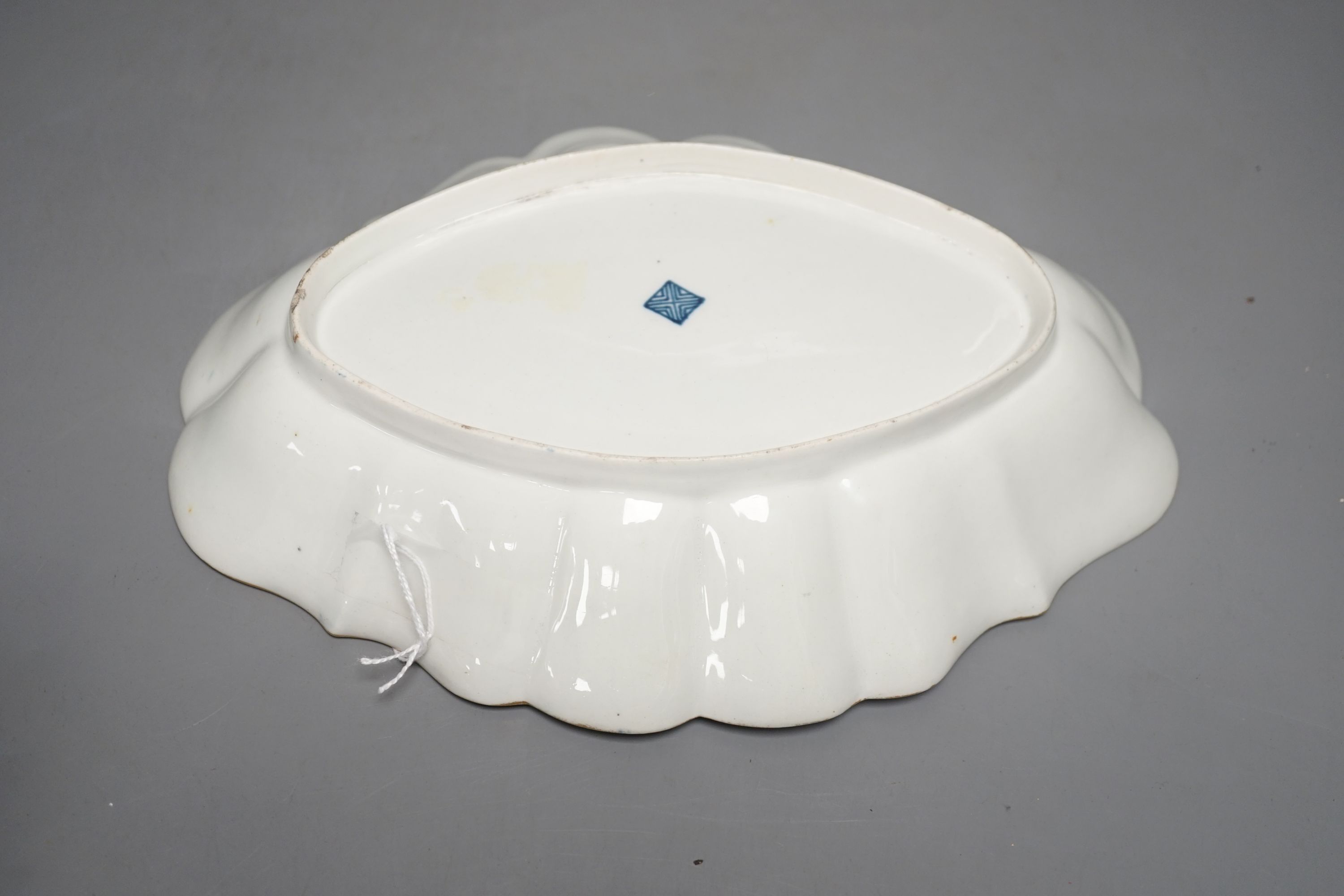 A Worcester scalloped oval dish with blue scale ground painted in kakiemon style with oriental flowers in git panels c.1768, 25 cms wide.